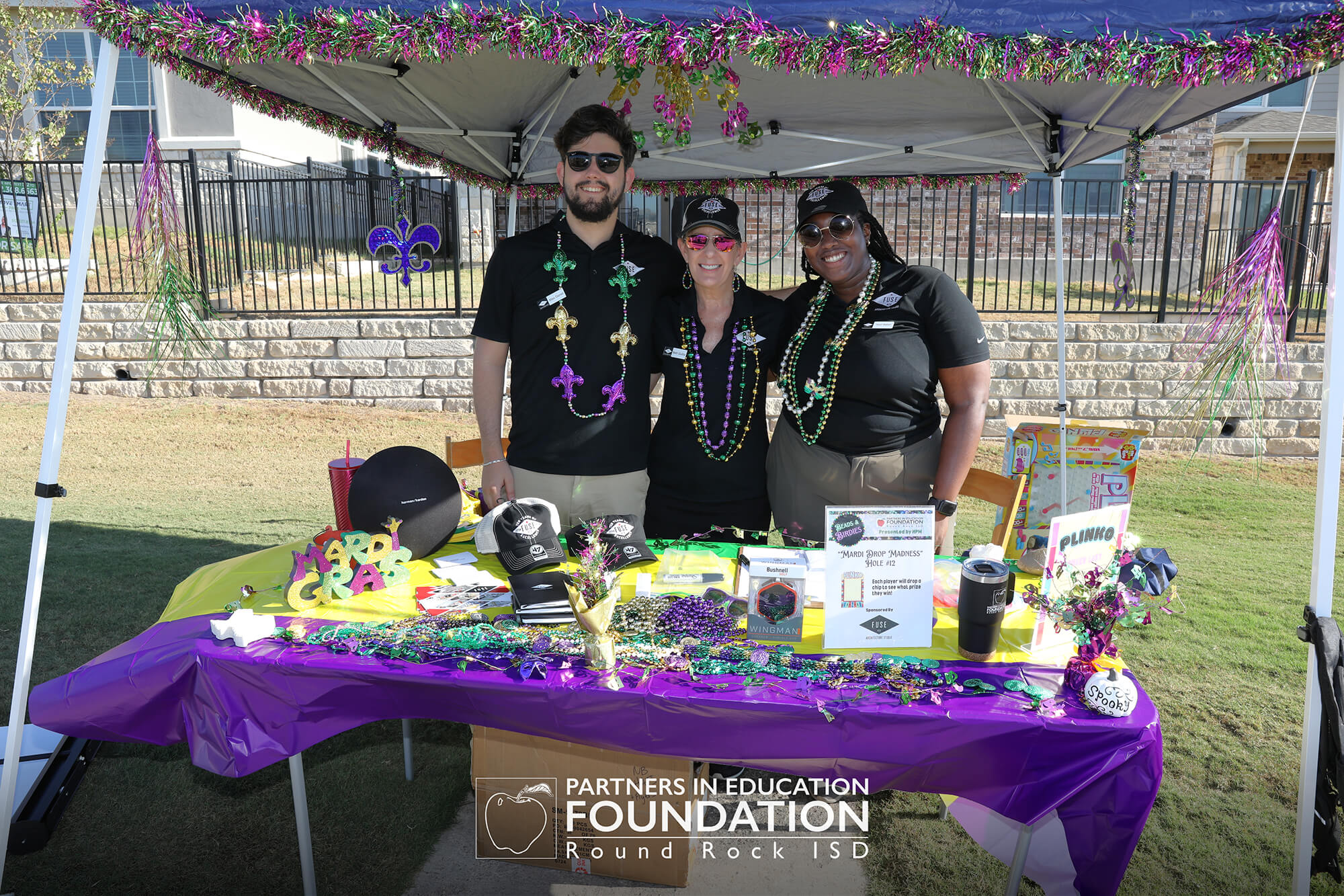 Three people at a decorated outdoor booth, showcasing products and information at a community event.